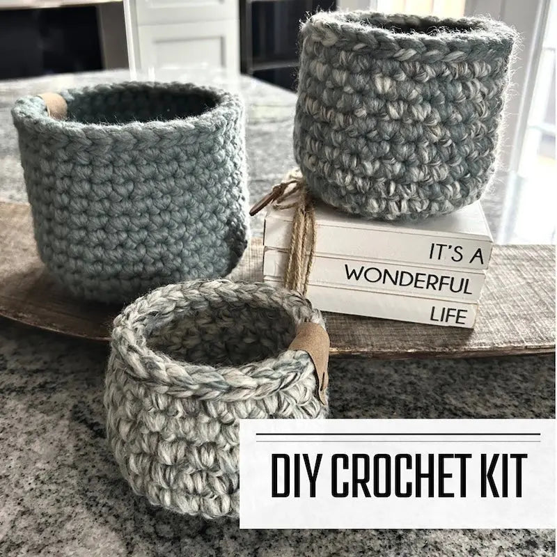 A crochet kit for a set of 3 storage baskets. The baskets are sitting on a wooden board on a counter.