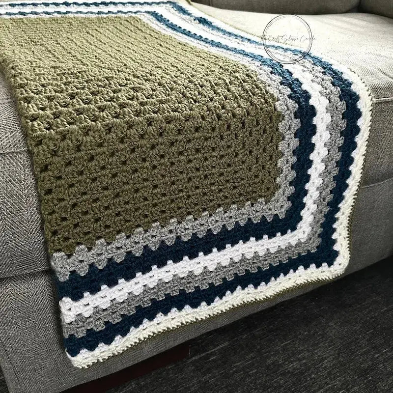 The finished granny square blanket, from this crochet kit, is lying across a couch.