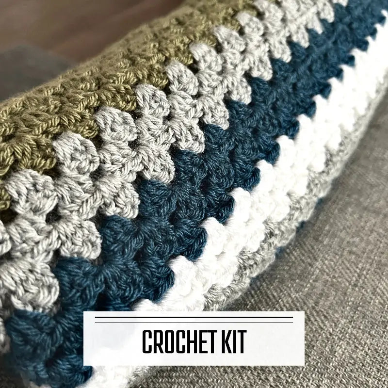 A DIY crochet kit for a couch throw or baby blanket. The finished blanket is rolled up on a couch.
