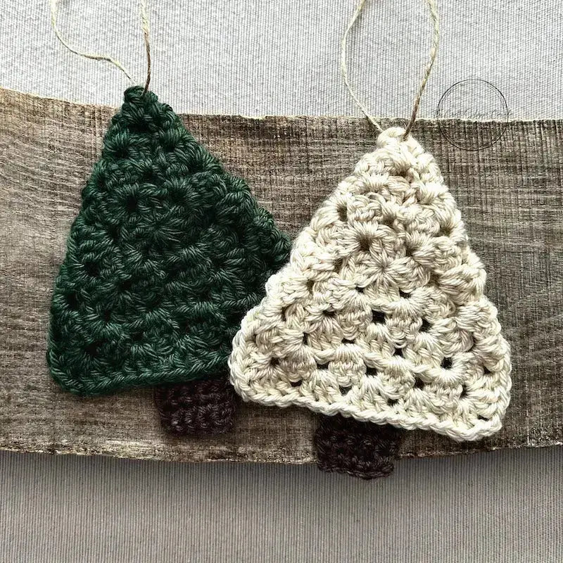 A green and ivory Christmas tree ornament, made from this crochet kit, are sitting on a wooden board.