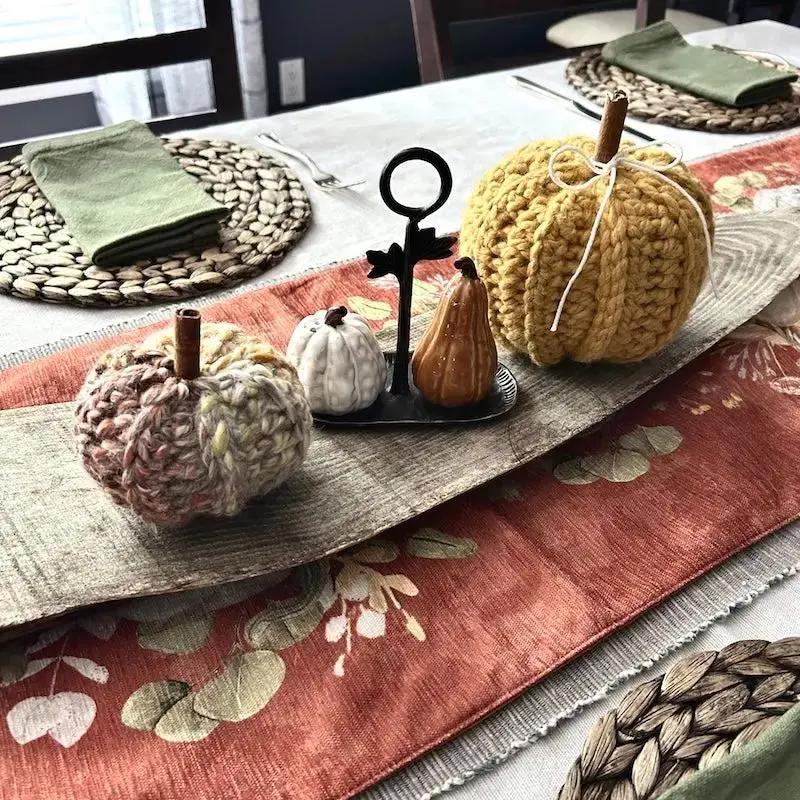 2 autumn pumpkins, made from this crochet pattern, are sitting on a Thanksgiving table.