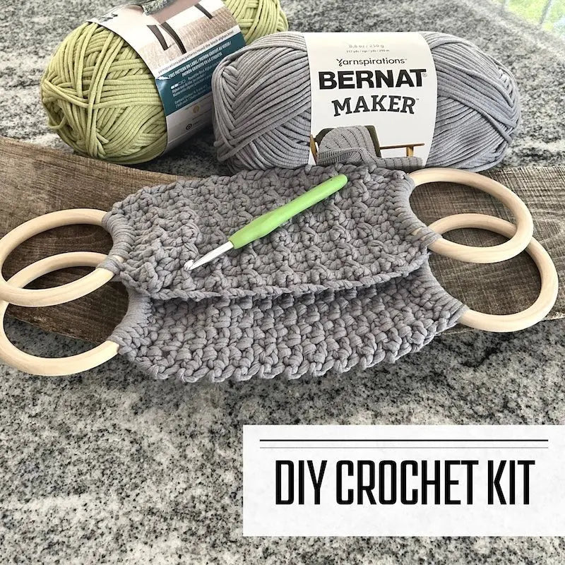 A DIY crochet kit for a tea towel holder. The holders are sitting on a wooden board with yarn and a crochet hook.