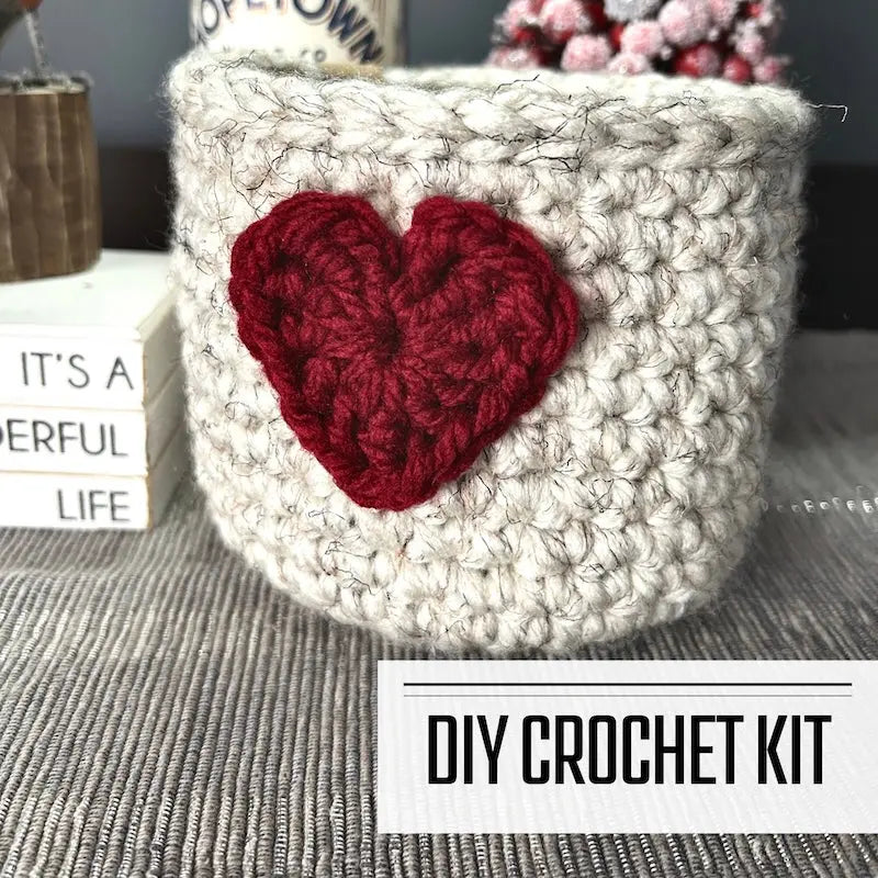 A crochet kit for a Valentine heart basket. The basket is sitting on a buffet with a spring bird beside it.