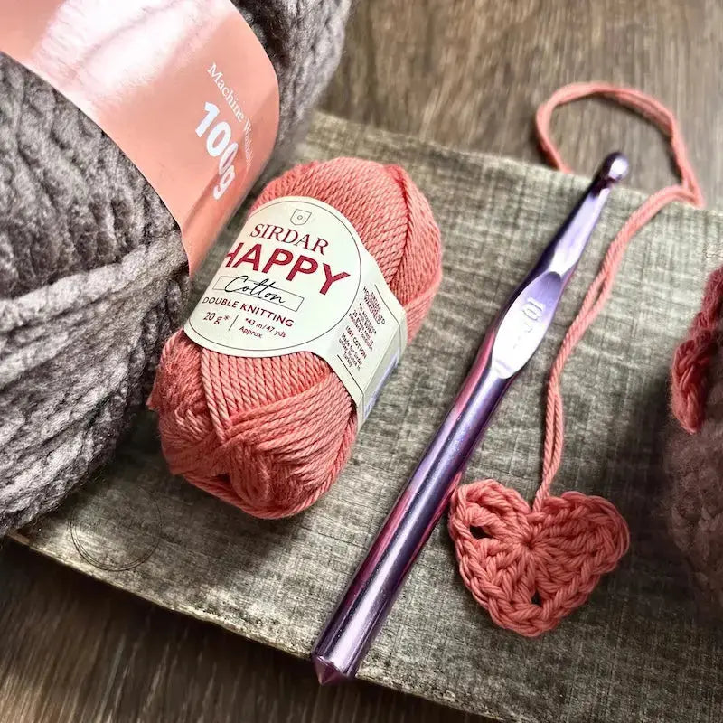 The yarn and hook, used in this crochet pattern is sitting on a wooden board.