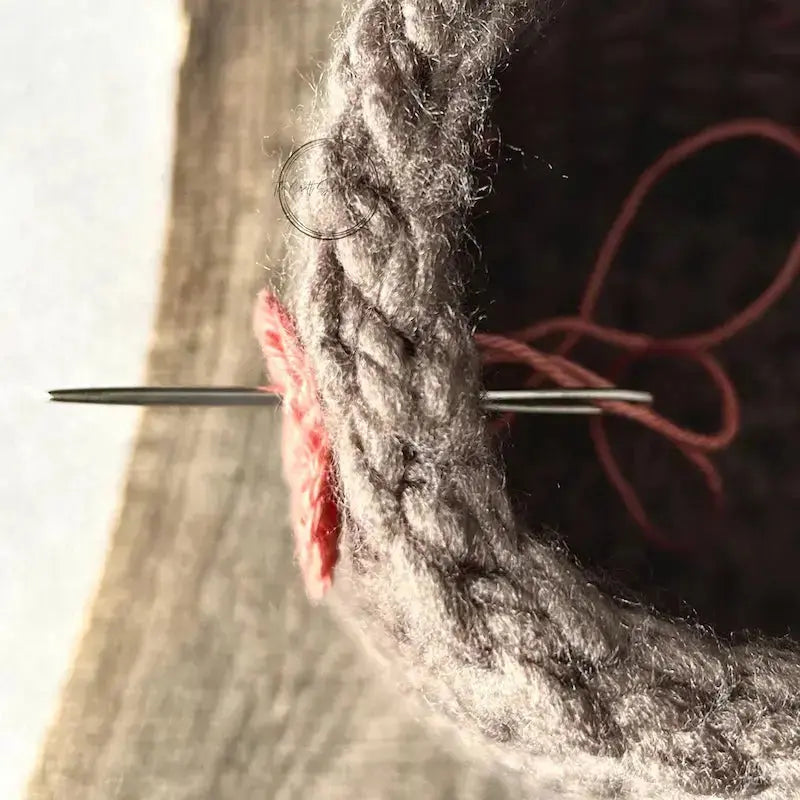 A crochet heart, made from this crochet pattern, is being sewn onto the crocheted basket.