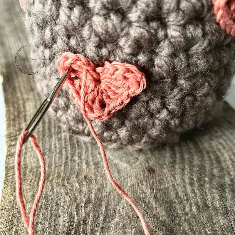 A crochet heart, made from this crochet pattern, is being sewn onto the crocheted basket.