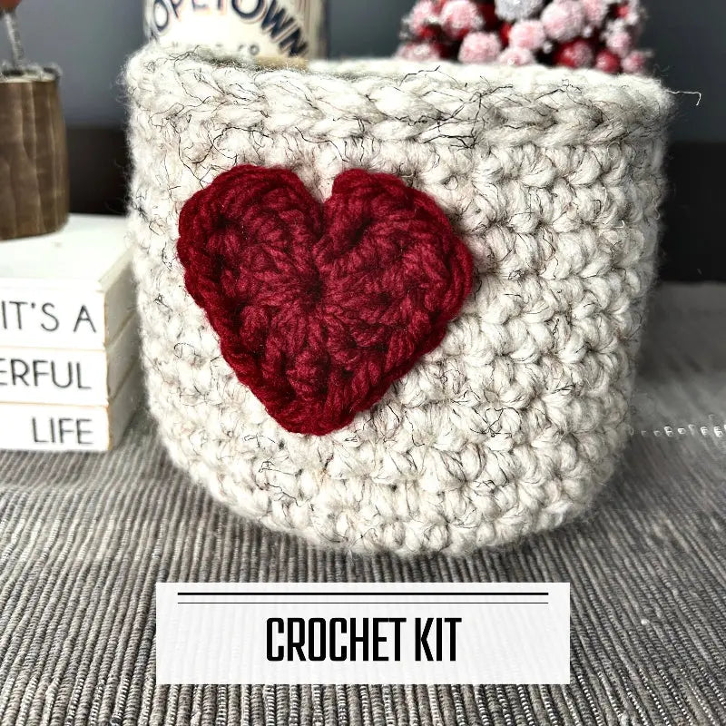 A crochet kit for a Valentine heart basket. The basket is sitting on a buffet with a spring bird beside it.
