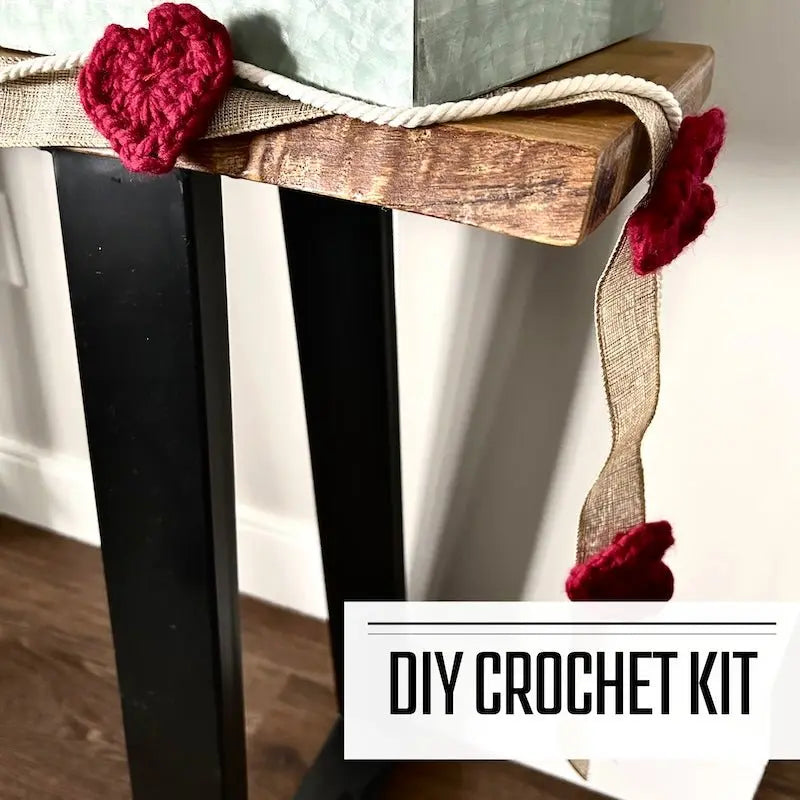 A crochet kit for a Valentine heart garland. The finished garland is hanging over a table.