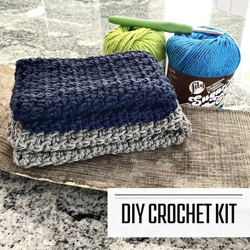 A DIY crochet kit for a dishcloth washcloth. The washcloths are sitting on a wooden board with yarn and a crochet hook.