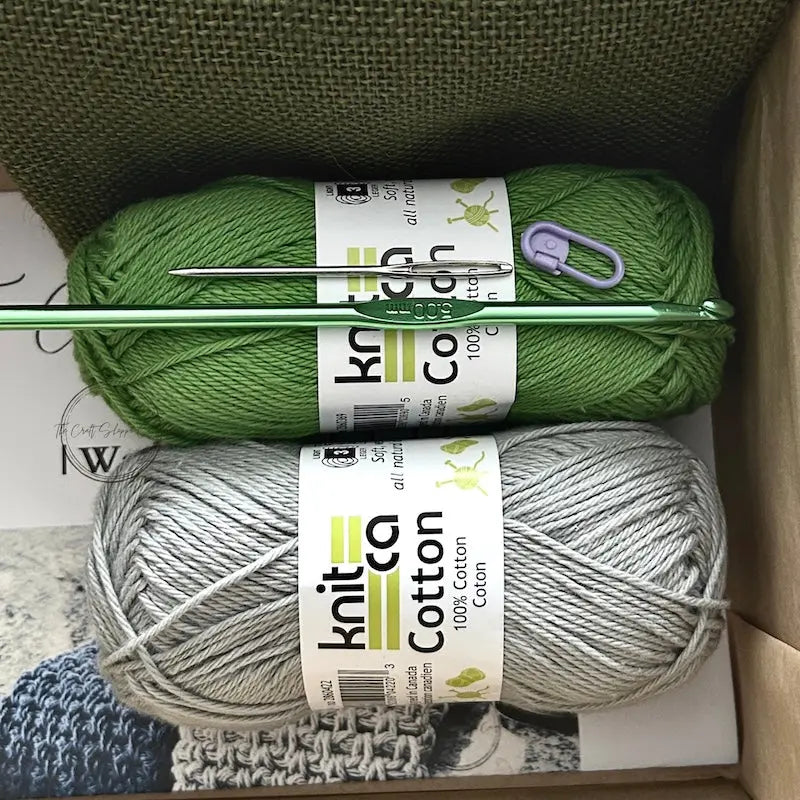 The yarn used in this crochet pattern is lying in a box with a crochet hook, stitch marker and a tapestry needle.