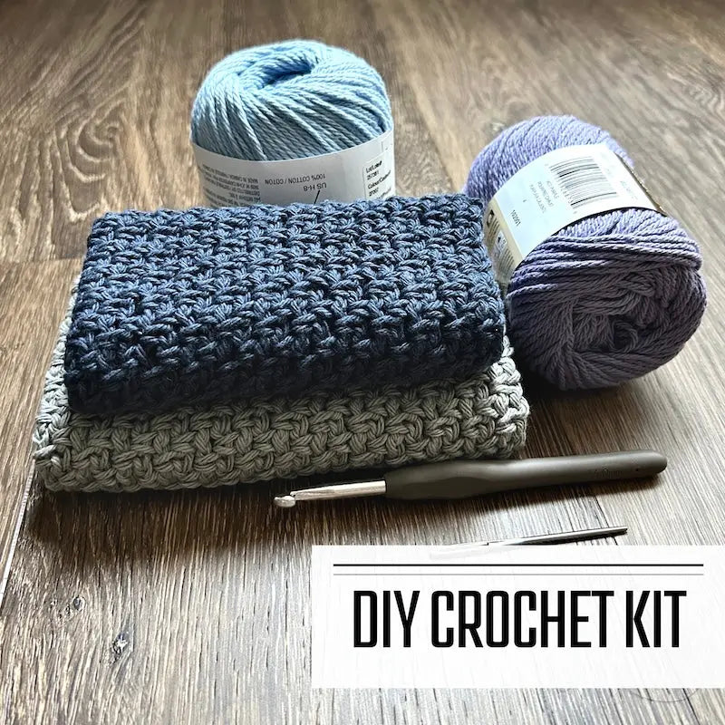 A DIY crochet kit for a dishcloth washcloth. The finished washcloths are sitting on a floor with yarn and a crochet hook.