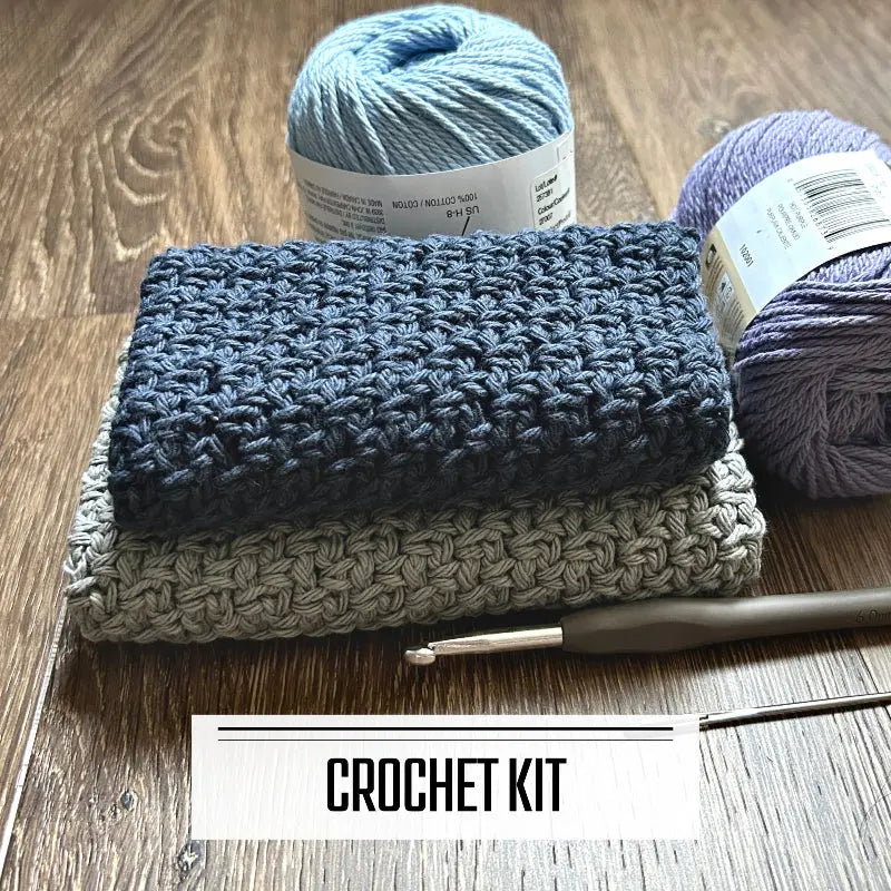 A DIY crochet kit for a dishcloth washcloth. The finished washcloths are sitting on a floor with yarn and a crochet hook.
