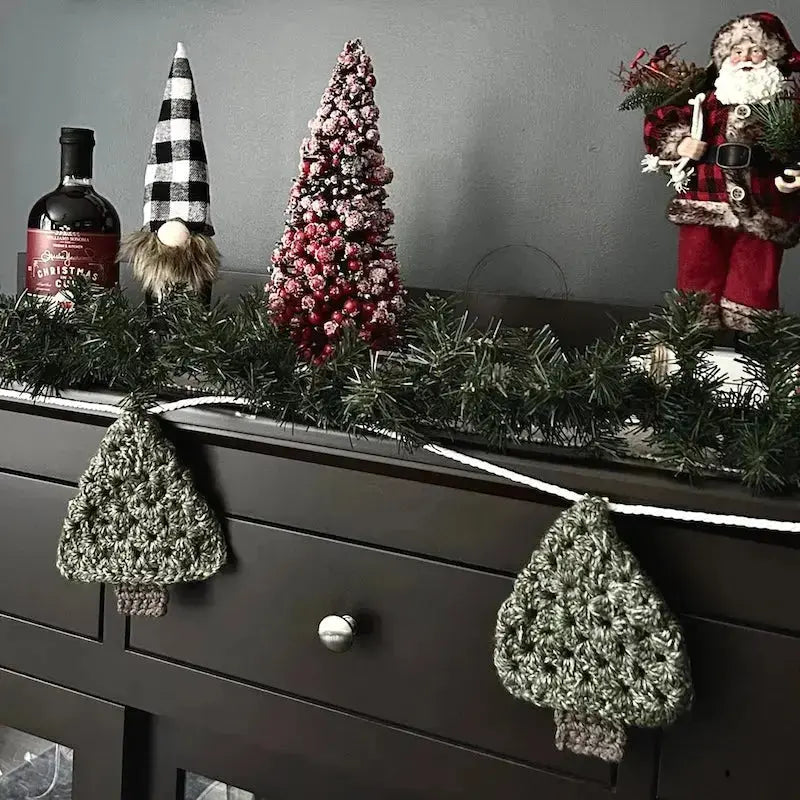 The Christmas garland, made from this crochet pattern, is hanging off of a buffet with Christmas decorations behind it.