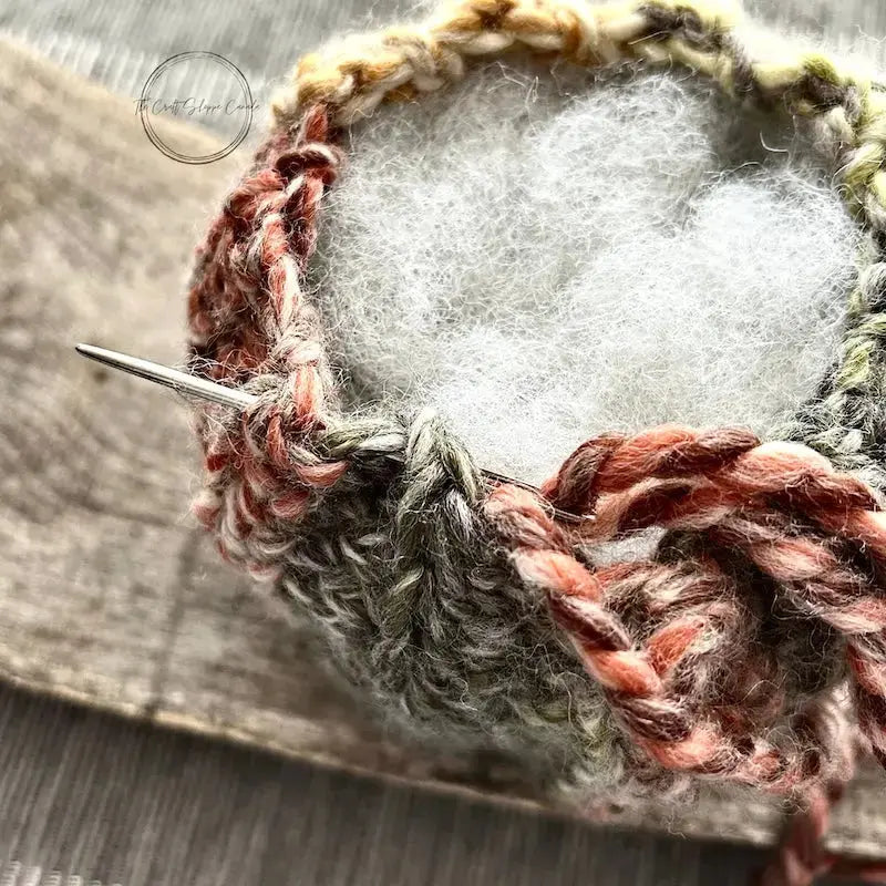 A close up of the top of the pumpkin, made from this crochet kit, to show the stuffing inside with a tapestry needle closing up the top.
