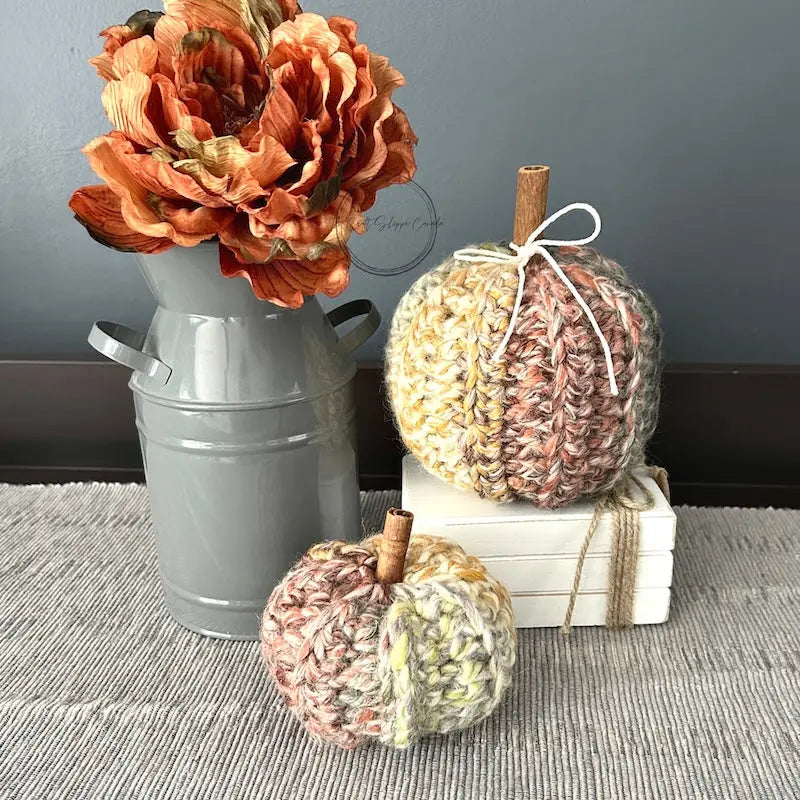 2 autumn pumpkins, made from this crochet pattern are sitting on a buffet with a vase of fall flowers beside them.