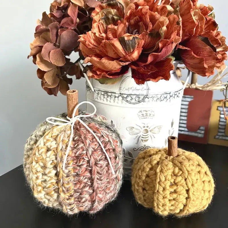 2 autumn pumpkins, made from this crochet pattern, are sitting on a table beside a fall floral arrangement.