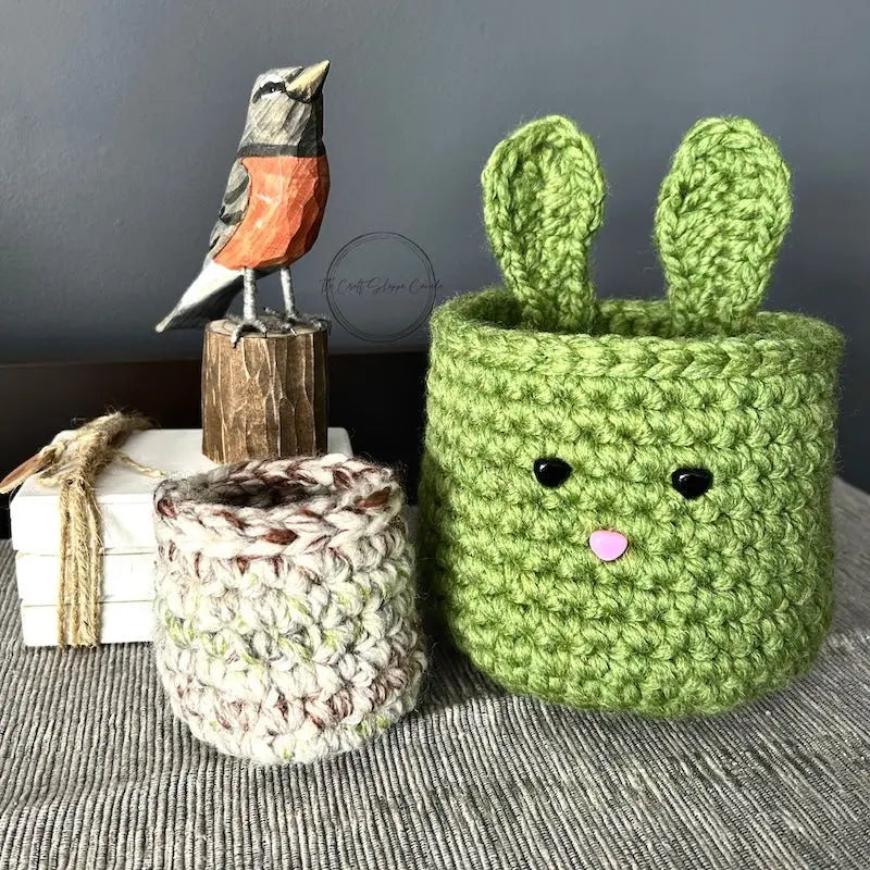 The Easter basket set, made from this crochet pattern, is sitting on a buffet with a spring bird beside it.