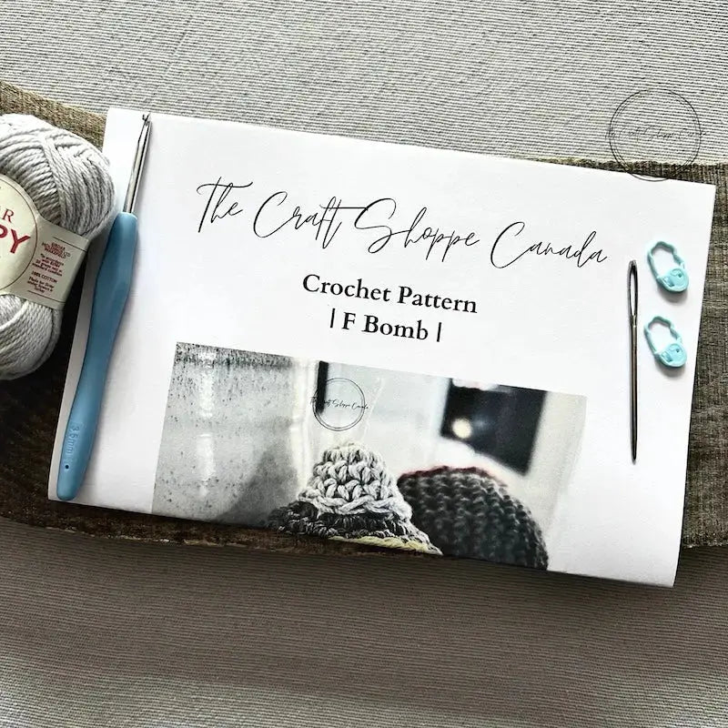 The pattern for this crochet kit is lying on a wooden board with yarn, a crochet hook, and a tapestry needle.