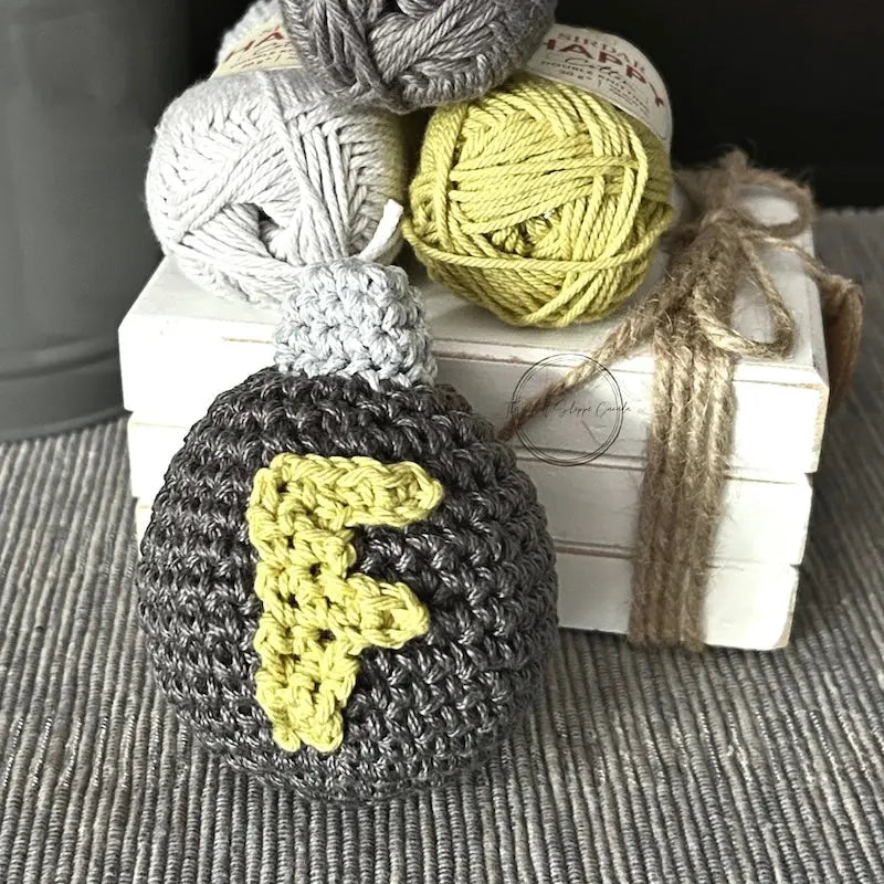 The F bomb, made from this crochet pattern is sitting on a table with yarn on a wooden board.