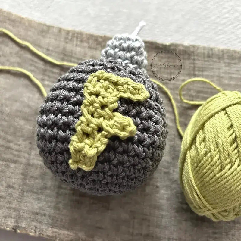 A close-up of the F-Bomb plush, made from this crochet kit, sitting on a wooden board with a ball of yarn.