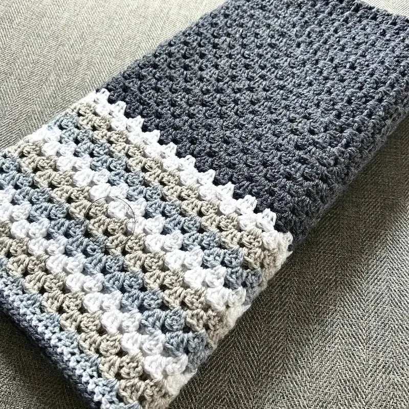 The finished granny square blanket, made from this crochet kit, is lying across a couch.