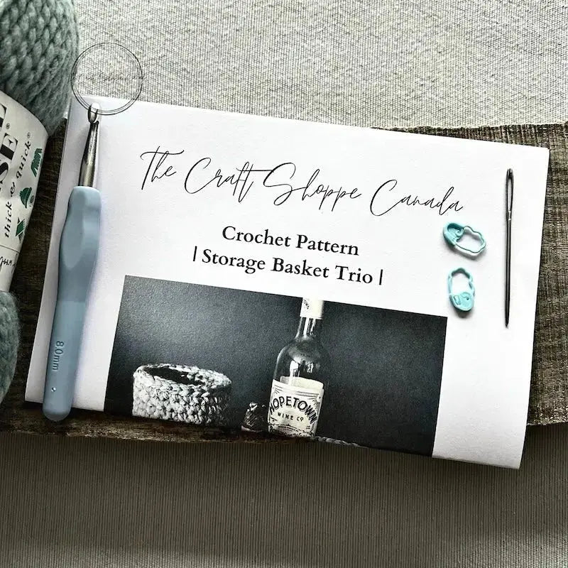 The pattern for this crochet kit is lying on a wooden board with yarn, a crochet hook, and a tapestry needle.