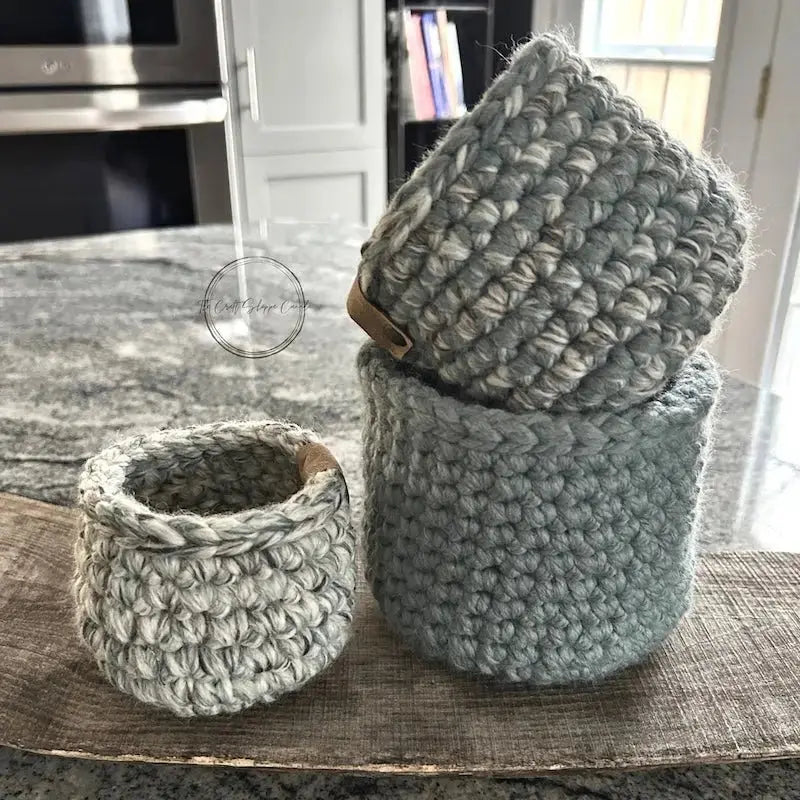 The storage baskets, from this crochet kit, are sitting on a wooden board on top of a counter.