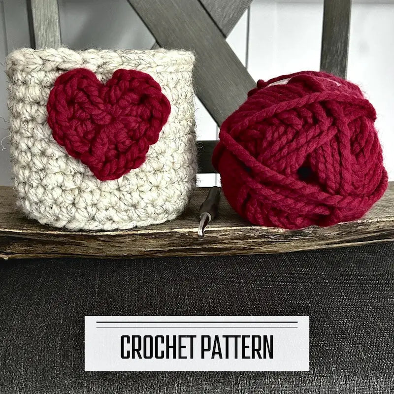 A digital PDF crochet pattern for a Valentine heart basket. The basket is sitting on a wooden board with a ball of yarn.