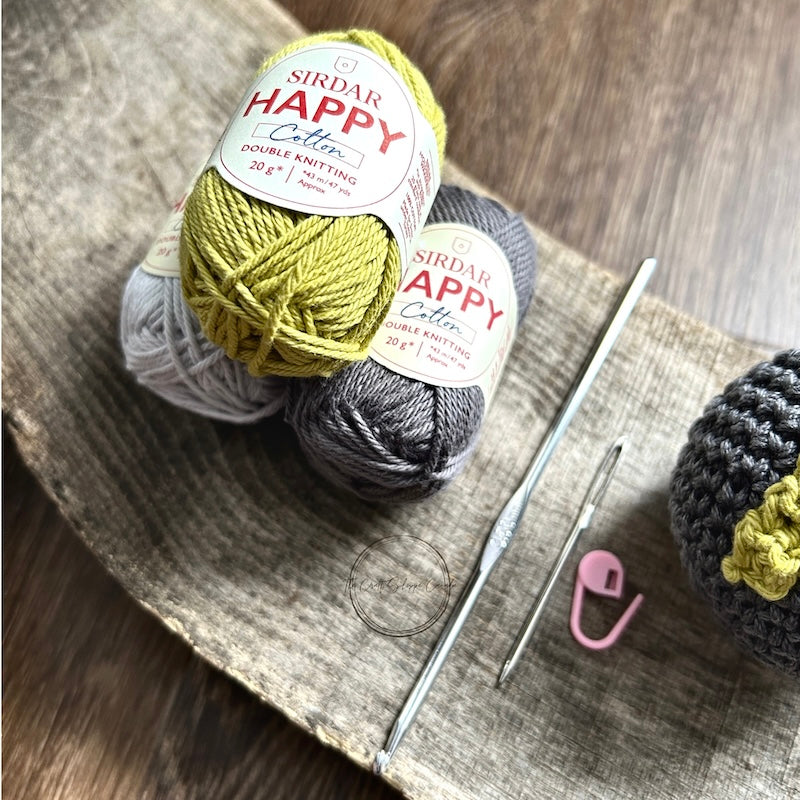 The yarn, used in this crochet kit is sitting on a wooden board with a crochet hook.