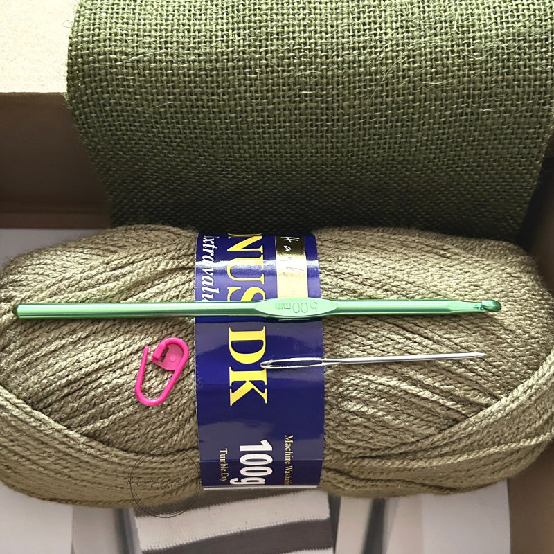 The yarn used in this crochet kit is lying in a box with a crochet hook, stitch marker and a tapestry needle.