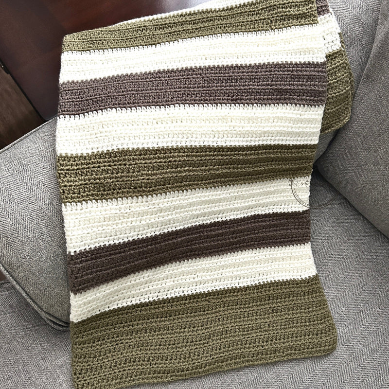 The finished baby blanket, made from this crochet kit, is draped over a couch.