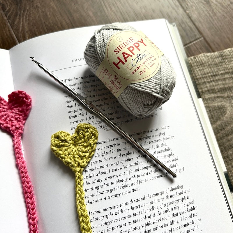 The finished bookmarks, made from this crochet kit, are lying on a board with yarn and crochet hooks.
