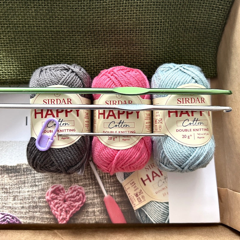 The yarn, used in this crochet kit, are lying in a box with the pattern and crochet hooks.