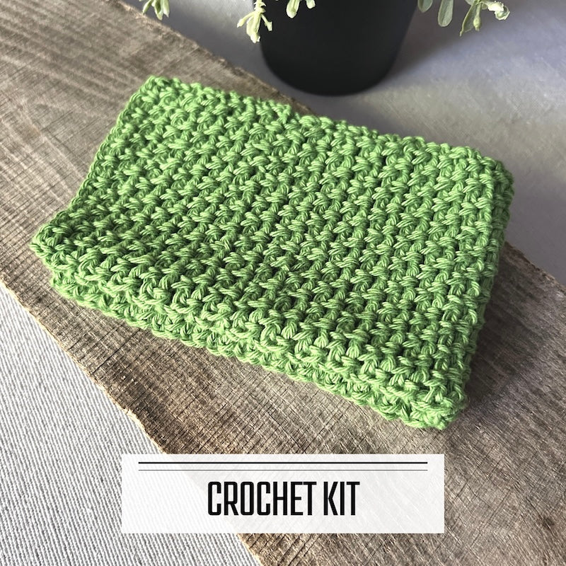 A DIY crochet kit for a dishcloth washcloth. The finished washcloth is sitting on a wooden board.
