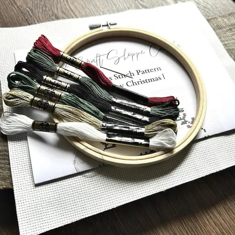 The tools needed to make this cross stitch pattern, are sitting on a wooden board with the pattern.