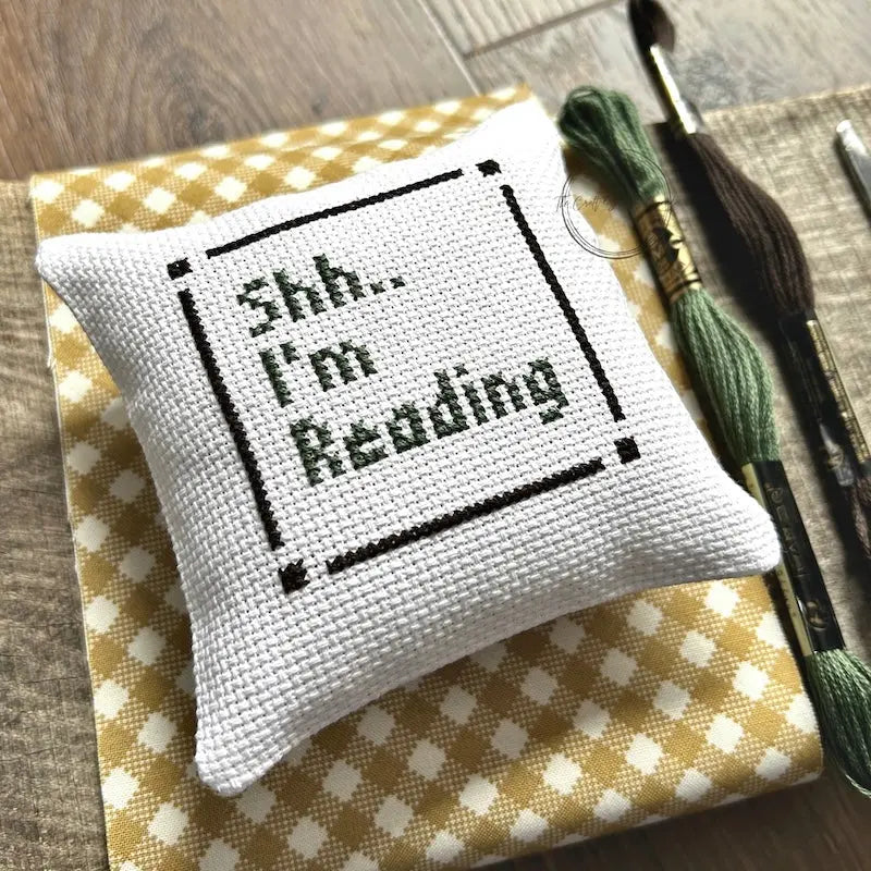 The finished pillow, made from this cross stitch kit, is sitting on a wooden board.