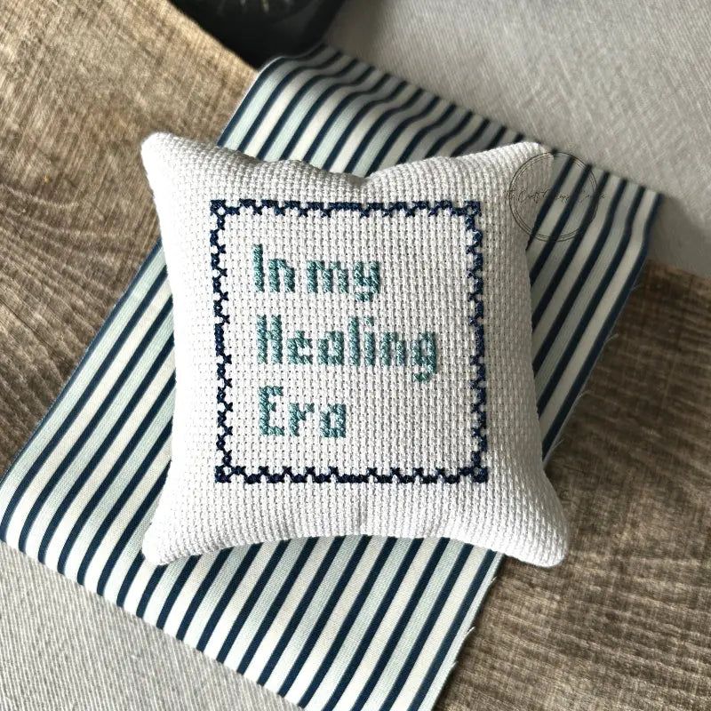 The finished pillow, made from this cross stitch kit, is sitting on a wooden board.