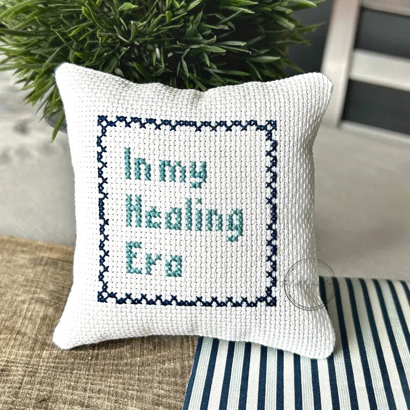 The finished pillow, made from this cross stitch kit, is sitting on a wooden board.