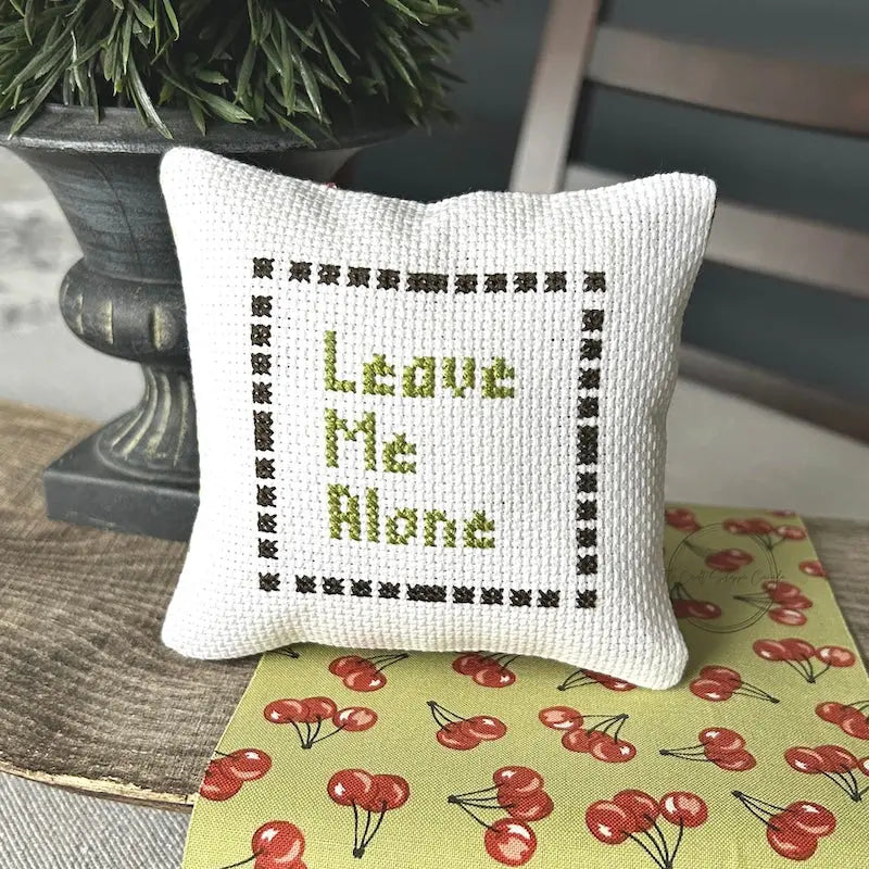 The finished pillow, made from this cross stitch kit, is sitting on a wooden board.