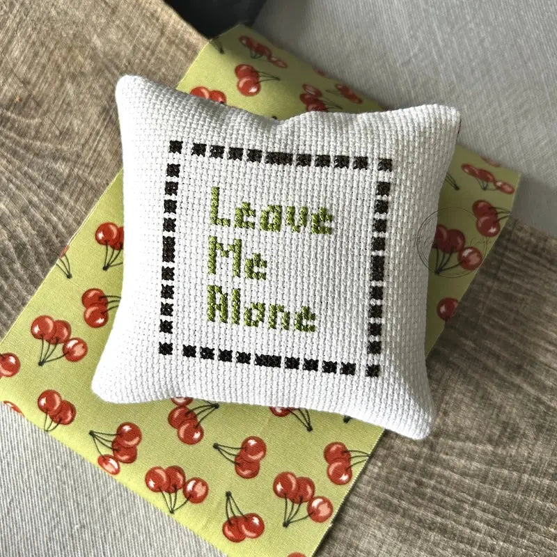 The finished pillow, made from this cross stitch kit, is sitting on a wooden board.