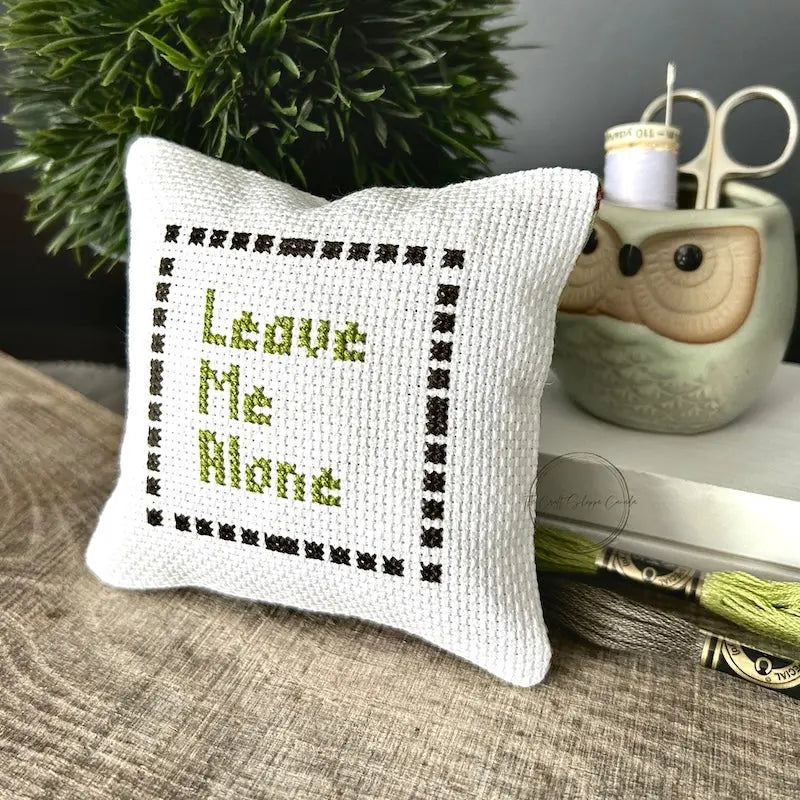 The finished pillow, made from this cross stitch kit, is sitting on a wooden board.