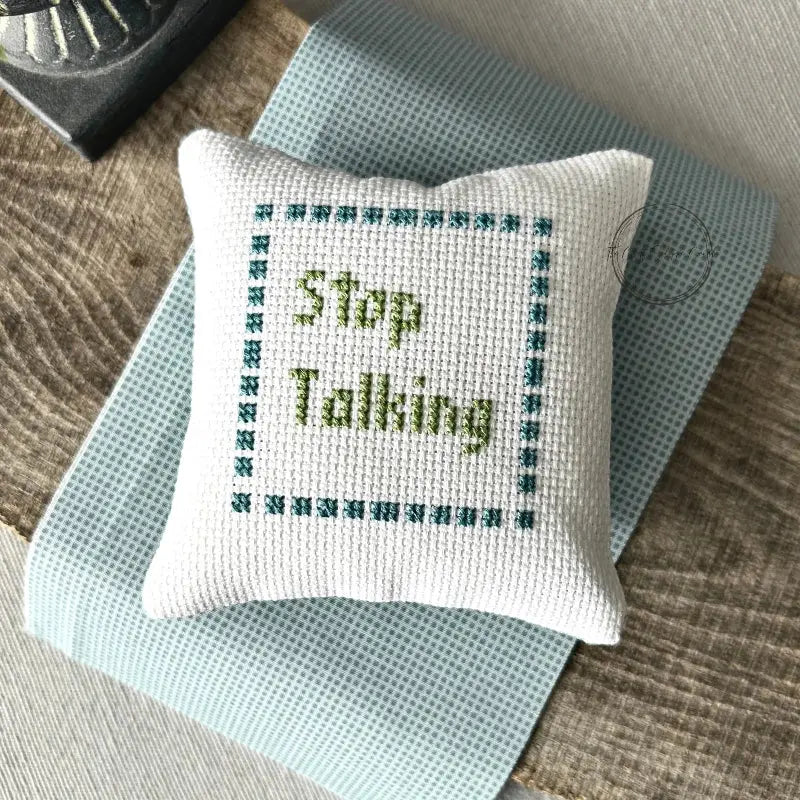 The finished pillow, made from this cross stitch kit, is sitting on a wooden board.
