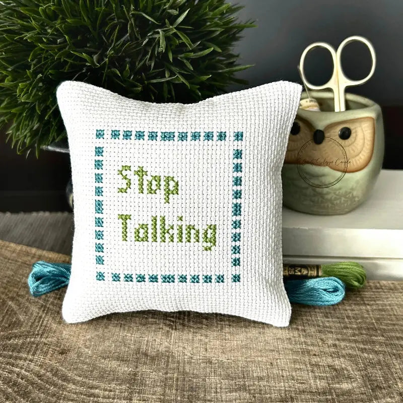 The finished pillow, made from this cross stitch kit, is sitting on a wooden board.