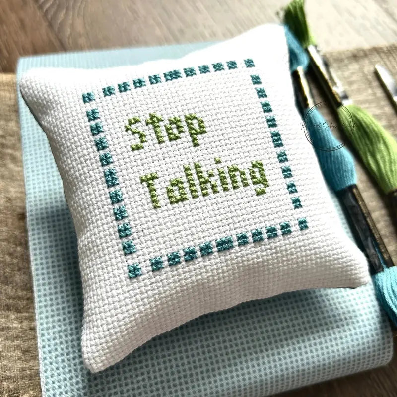 The finished pillow, made from this cross stitch kit, is sitting on a wooden board.