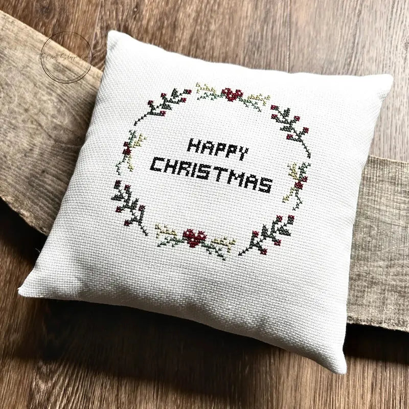 The finished pillow, made from this cross stitch pattern, is sitting on a wooden board.