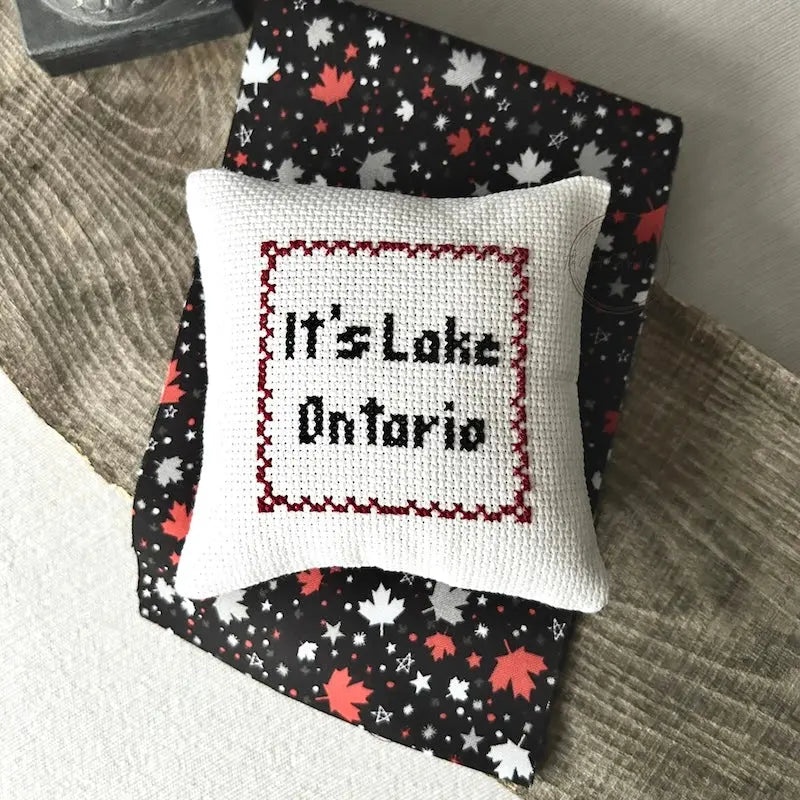 The finished pillow, made from this cross stitching kit, is sitting on a wooden board.