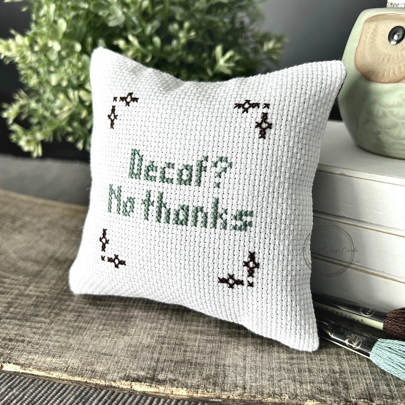 The finished pillow, made from this cross stitch kit, is sitting on a wooden board.