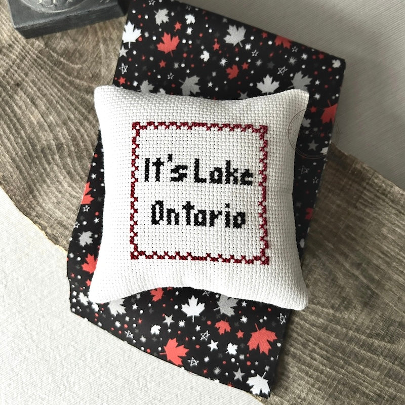 The finished pillow, made from this cross stitching kit, is sitting on a wooden board.