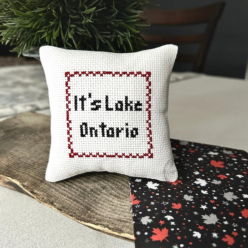 The finished pillow, made from this cross stitching kit, is sitting on a wooden board.