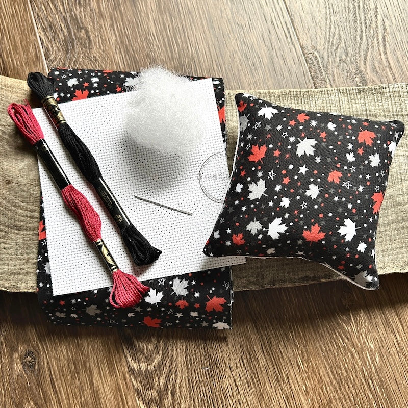 The supplies included in your cross stitch kit are sitting on a wooden board.